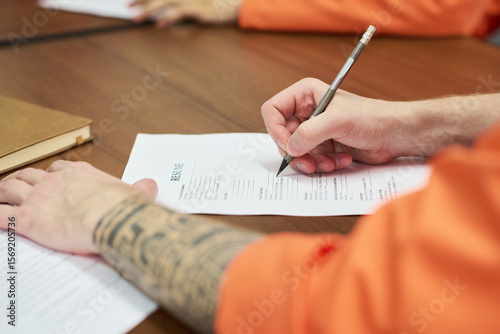 Billede på lærred Caucasian young adult man with tattooed arm filling out resume form at desk duri