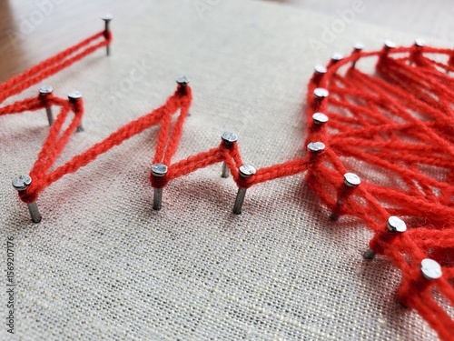 Creative string art project featuring vibrant red yarn and nails on fabric, depicting geometric patterns in numerous shapes and lines, showcasing artistic expression and craftsmanship skills