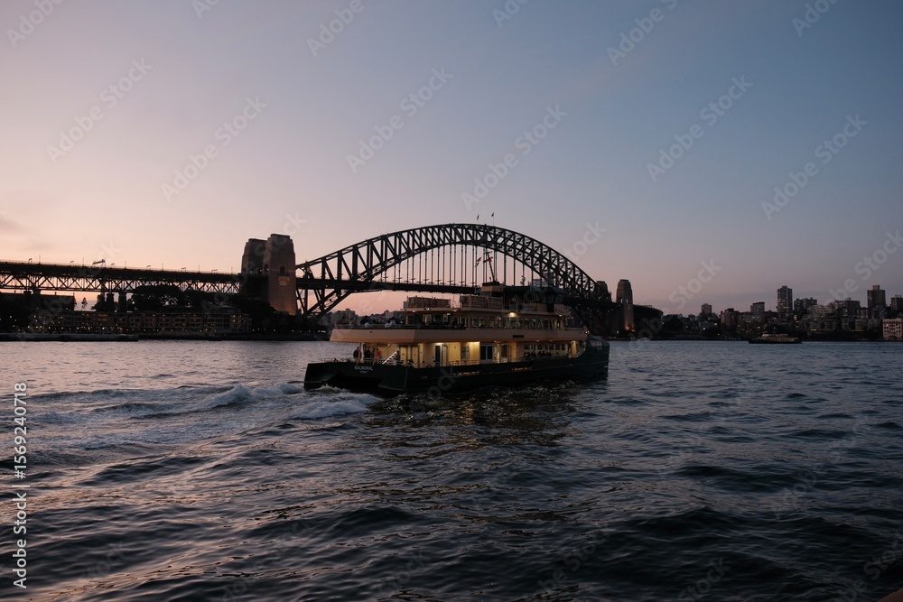 Fototapeta premium Sydney, Australia - August 10th 2024 - The iconic Sydney Harbour Bridge frames a cruising vessel. Perfect for travel brochures, website headers, or evoking Australian wanderlust.