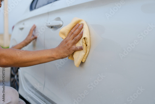 A smiling man is washing his car with soapy water under bright sunlight, showing his enthusiasm and joy in his daily work.
