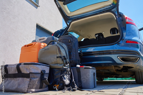 Suitcases and bags in front of open car trunk, standing on pavement near suburban house. Luggage ready for loading in vehicle before travel or moving. Concept of relocation or road trip