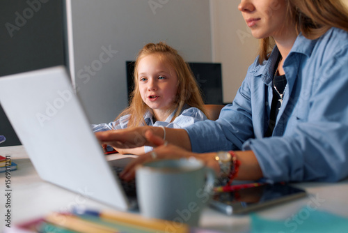 A schoolgirl sits with her mother and carefully studies a video lesson on a laptop