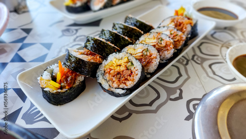 A plate of seaweed rice rolls or gimbap with vibrant fillings served on a patterned table, traditional local South Korean dish