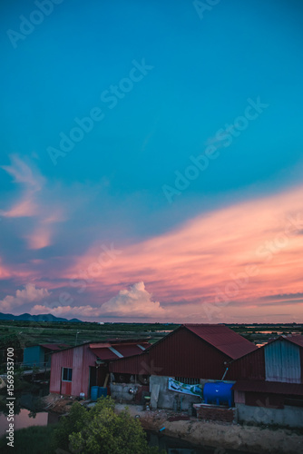 Peaceful dusk scene with colorful sky casting hues over tin rooftops that a candid scene of daily life in the rural countryside of Kampot, Cambodia