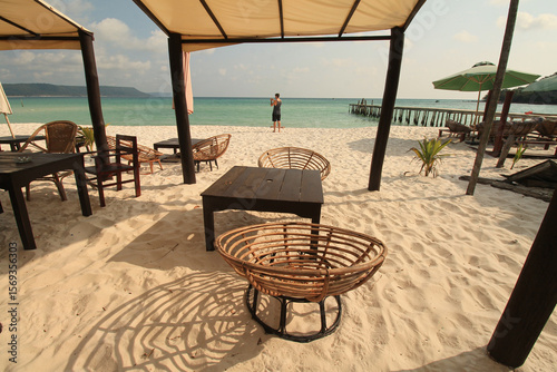 Obraz na płótnie Seating area under a canopy on a sunny beach with a person enjoying the ocean vi