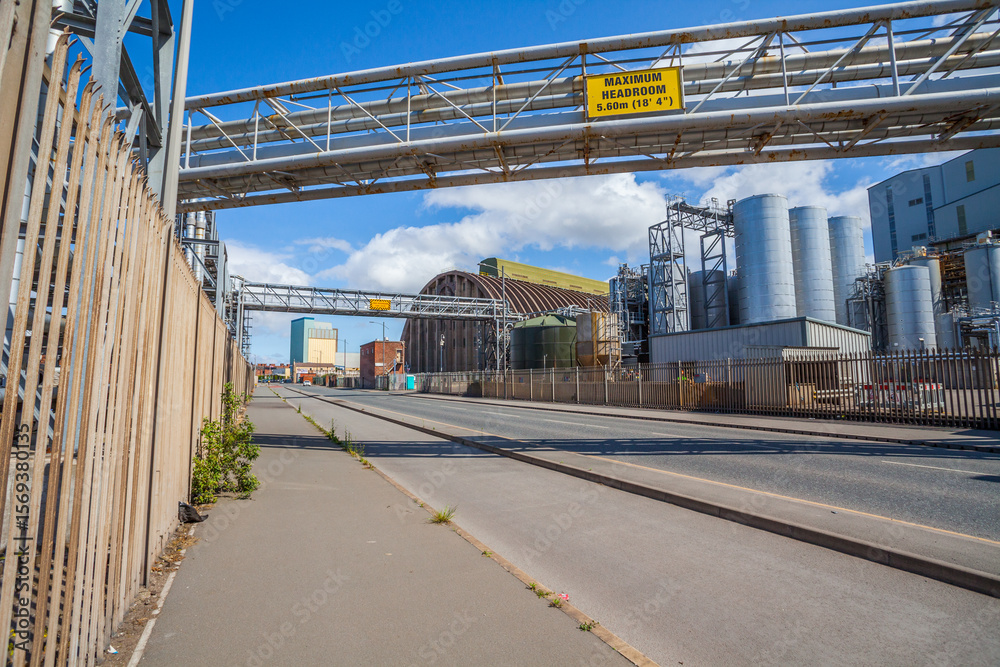 Fototapeta premium Weathered industrial tanks and scaffolding stand against a cloudy sky. An active site displaying signs of age, ongoing maintenance, and sustained operational use