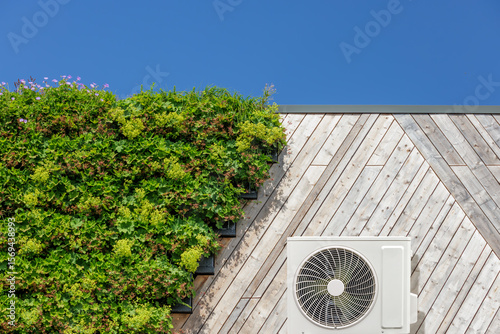 Air-source heat pump on a green sustainable building covered with blooming vertical hanging plants