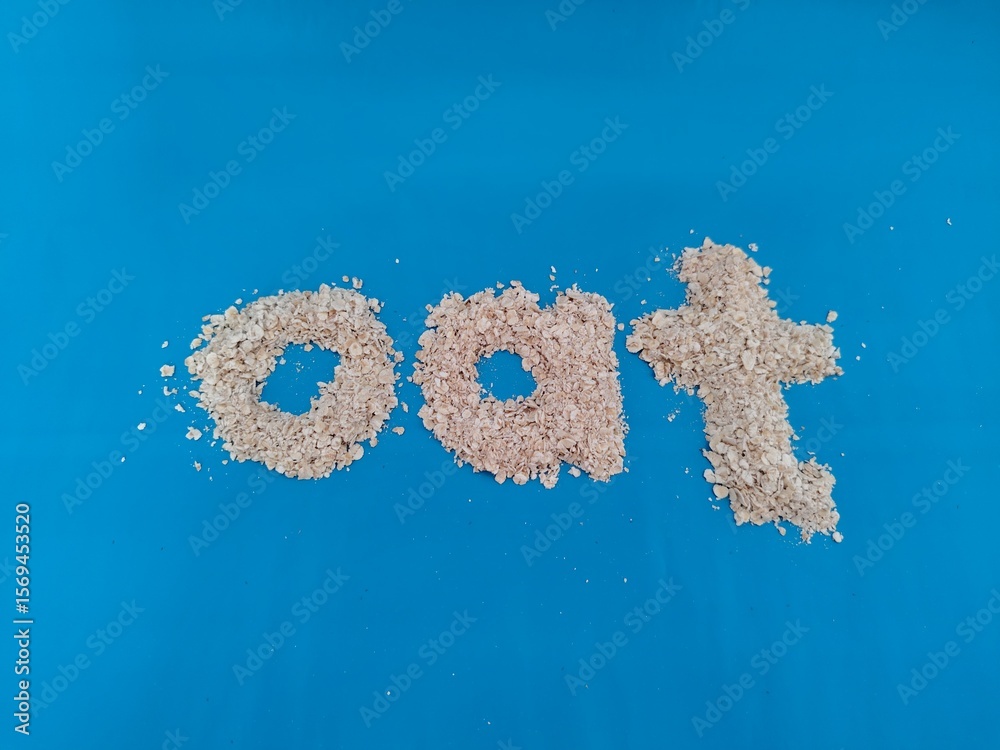 Fototapeta premium Word ‘oat’ spelled with raw oatmeal flakes on a vibrant blue background, symbolizing healthy breakfast and natural food ingredients. health, diet concept