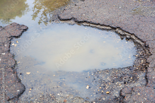Shallow water-filled pothole in weathered asphalt road surface