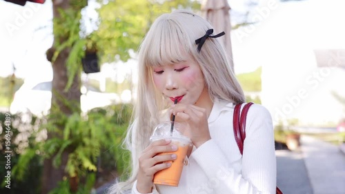 Young person enjoys refreshing drink outdoors, surrounded by vibrant greenery, conveying sense of casual enjoyment and relaxation