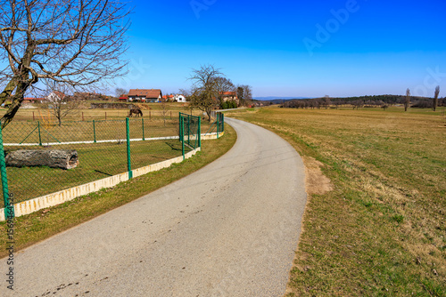 Curved rural road with fences and farmhouse in countryside landscape on sunny day