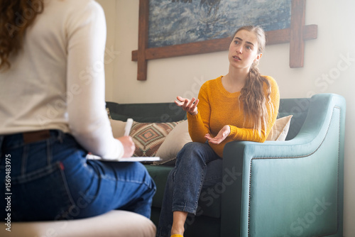 Foto Young woman talking to psychologist during therapy session, sitting on sofa, fem