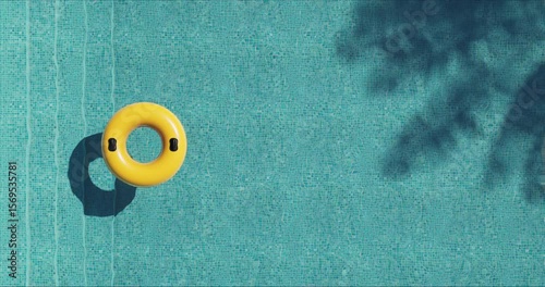 Top view of a vivid yellow inflatable ring floating on clear blue pool water. Sunlight and foliage cast shadows on the mosaic tiles. Calm, minimal scene evoking summer leisure and relaxation.