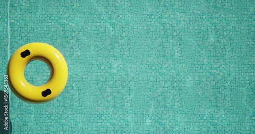 Top view of a bright yellow inflatable ring floating on clear turquoise water in a swimming pool. Sunlight casts a distinct shadow on the mosaic tiles. Minimal, peaceful summer vacation vibe