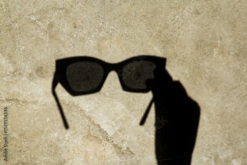 The shadow of sunglasses, cast on a textured wall, creates a unique and stylish image. A shadow of sunglasses is cast on a textured surface, showcasing a creative and artistic composition.