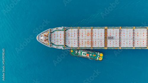 Aerial top view tugboat pushing container ship at blue sea.