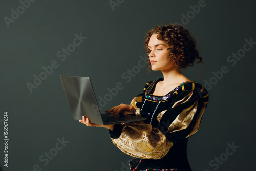 Portrait of a young aristocratic woman dressed in a medieval dress working on laptop