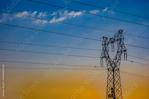 High voltage power towers and lines under the background of blue sky, white clouds, and orange sunlight