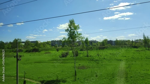 View from carriage window to natural expanses and small town. Fast-changing summer landscape seen from moving train