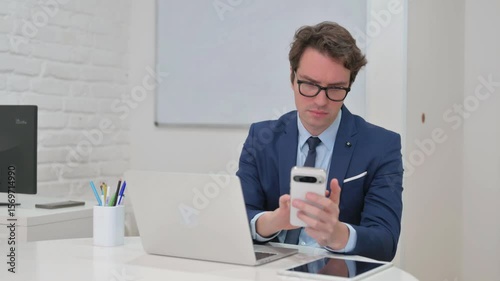 Mature Adult Businessman Using Phone and Laptop at His Desk