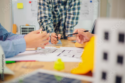 Engineers and architects discuss and consider construction plans for new renewable energy project in office with design documents, laptop and hard hat on table. Concept of engineers and architects+