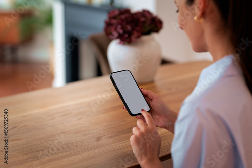 Woman sitting at a table and using a blank screen mobile phone