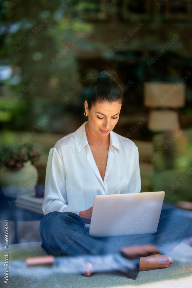 Fototapeta premium Brunette haired woman sitting at home and using her laptop