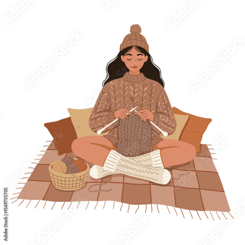 Young woman knitting by the cozy cushions on the plaid blanket  