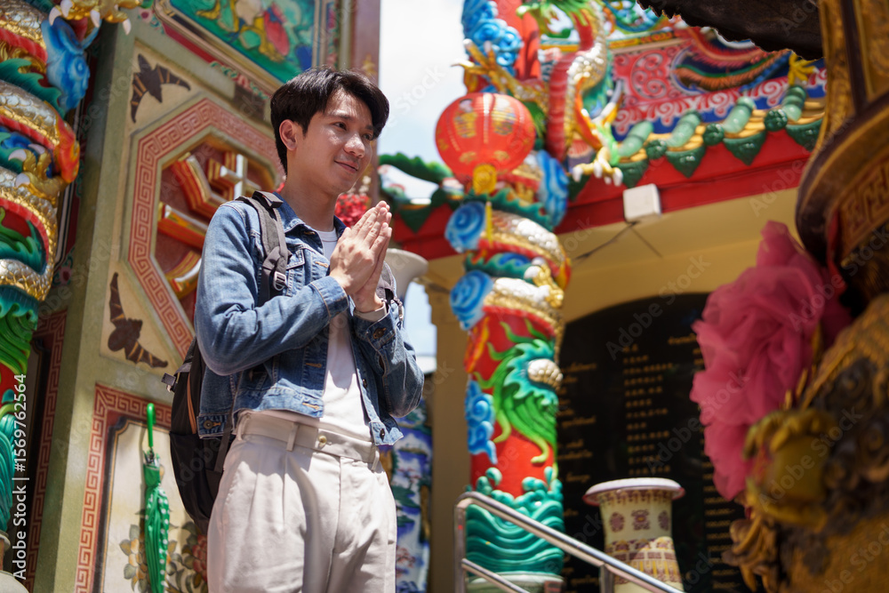 Obraz premium Young male traveler praying at a colorful Chinese temple during his cultural journey.