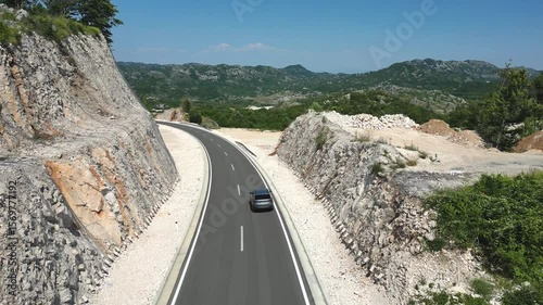 Car driving on mountain road surrounded by rocky slopes and green forests in Croatia, aerial view