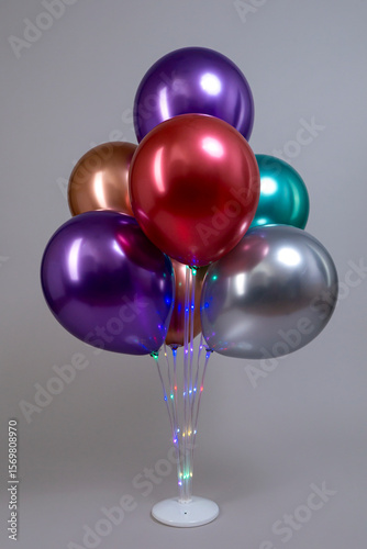 Multicolored metallic colored balloons on white plastic luminous stand isolated on gray background