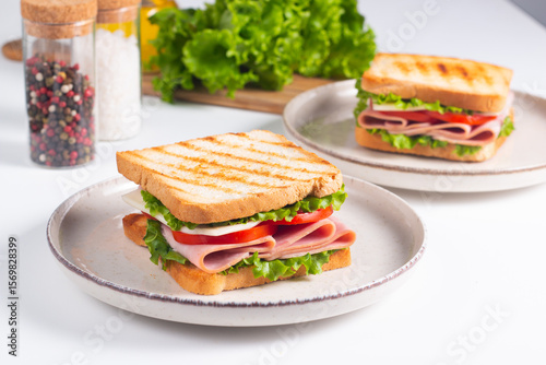 Close-up of two sandwiches with bacon, salami, prosciutto and fresh vegetables on rustic wooden cutting board. Club sandwich concept