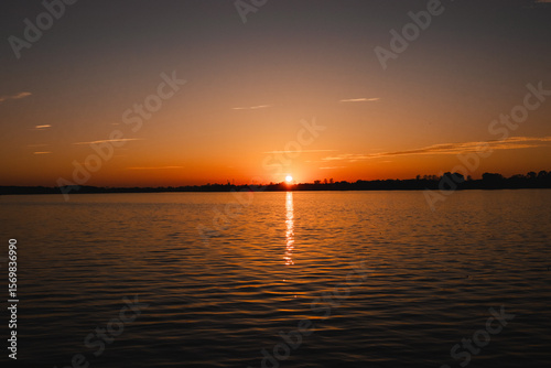 A breathtaking red sunset over a tranquil lake, capturing the serene beauty of nature at dusk. The vibrant hues of crimson, orange, and gold reflect off the still water, creating a mirror-like surface