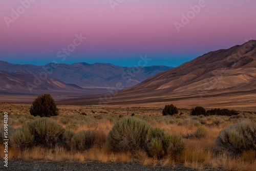 A minimalist desert landscape at sunset with a purple sky and distant silhouette of mountains.