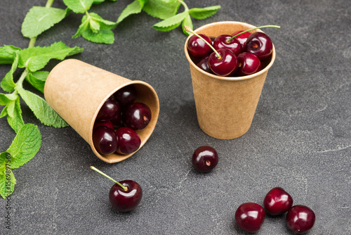 Ripe cherries in paper cups. Mint leaves on table
