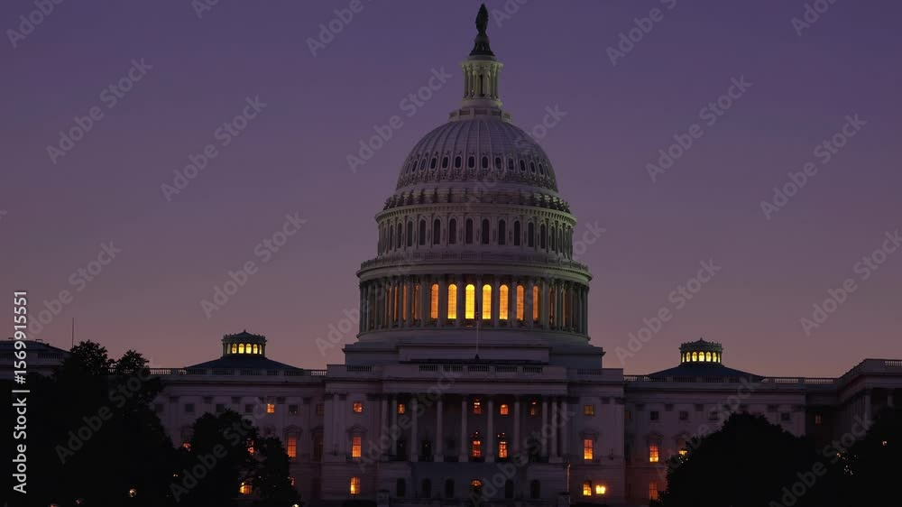 Silhouette of United States Capitol Building during twilight hours. Soft light glows from interior windows against dark sky in Washington D.C
