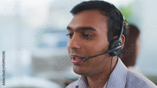 Confident Indian tech support operator seated at desk using headset and CRM tools. Communicating with clients in a multicultural company, providing business assistance and service.