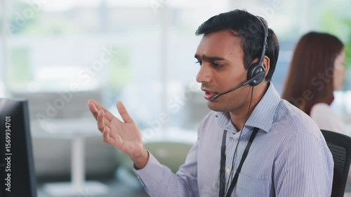 Confident Indian tech support operator seated at desk using headset and CRM tools. Communicating with clients in a multicultural company, providing business assistance and service.