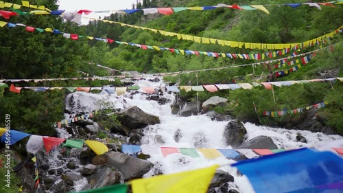 Slow motion shot of a water stream in the Himalayan mountains with prayer flags waving above it as seen near Triloknath village in Pattan valley, Himachal Pradesh, India. Scenic view of waterfall.