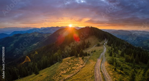 Offroad path crossing hill top. Dark dirt road illuminated with bright setting sun. Amazing sunset scenery in wild mountain forest. Beautiful nature landscape