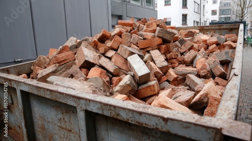 A large dumpster is filled with broken bricks and construction debris in an urban area
