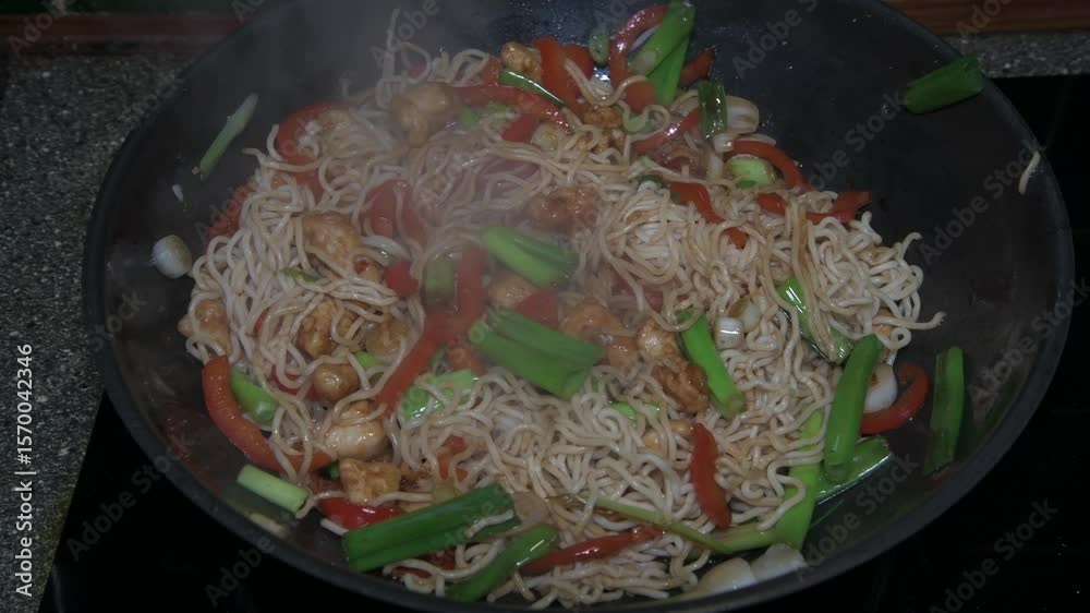 Sizzling chicken stir fry in a wok with chili, garlic noodles, red pepper, spring onion, soy sauce, and Shaoxing wine. Asian cooking in motion.