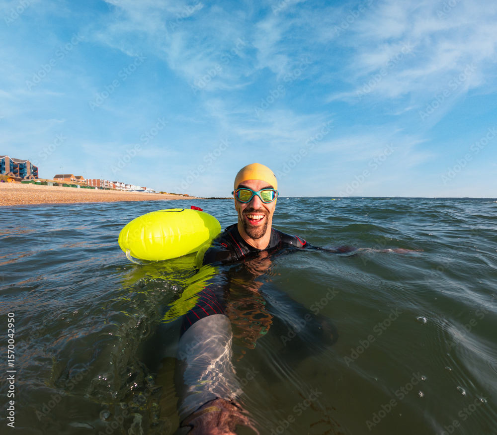 Fototapeta premium Triathlete swimming in open water with safety buoy and goggles