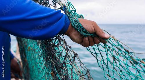 Fisherman’s hand gripping tangled green fishing nets aboard a boat at sea, representing traditional coastal labor.