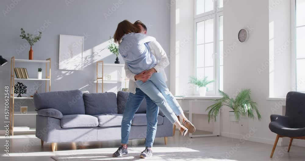Happy young couple dancing in modern living room to celebrate relocation to new own apartment, loving husband lifts his overjoyed wife, hugging, feels happy, start living together to enjoy marriage Happy young couple dancing in modern living room to celebrate relocation to new own apartment, loving husband lifts his overjoyed wife, hugging, feels happy, start living together to enjoy marriage