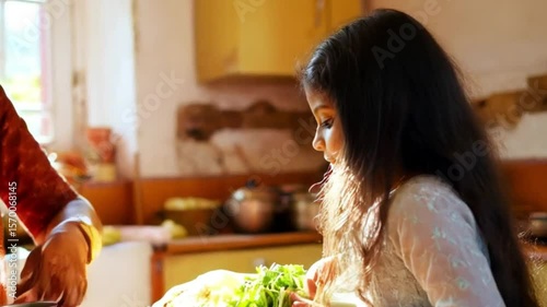Photo of an elderly indian woman and a young girl are busy preparing food together in a sunlit kitchen
