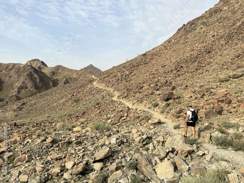 A lone hiker follows a rocky mountain trail near Hatta, UAE. This scene highlights eco-tourism and sustainable travel in the striking, arid landscapes of the Arabian Peninsula.