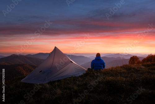 Hiker near his tent against the backdrop of an incredible sunset sky in autumn mountains. Landscape photography