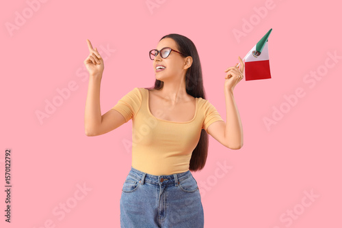 Young woman with Mexican flag pointing at something on pink background