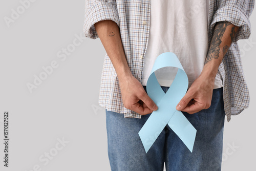 Murais de parede Young man with blue ribbon on light background, closeup